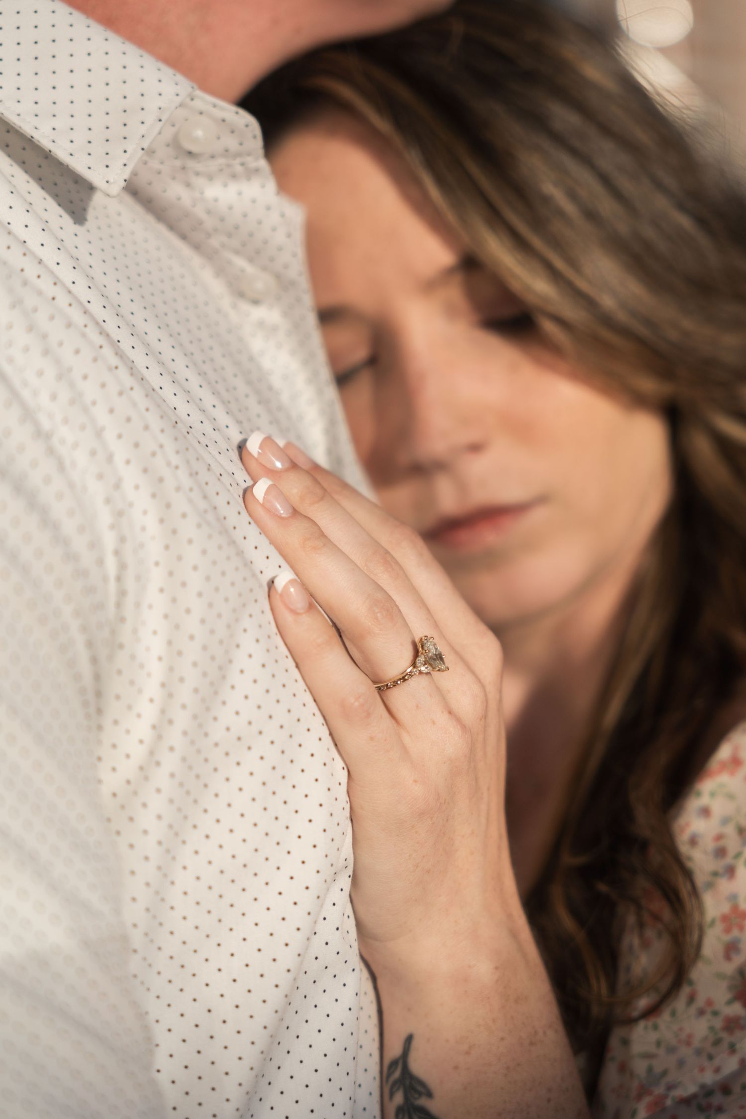 Woman with engagement ring resting her hand on a mans chest in a tender moment.