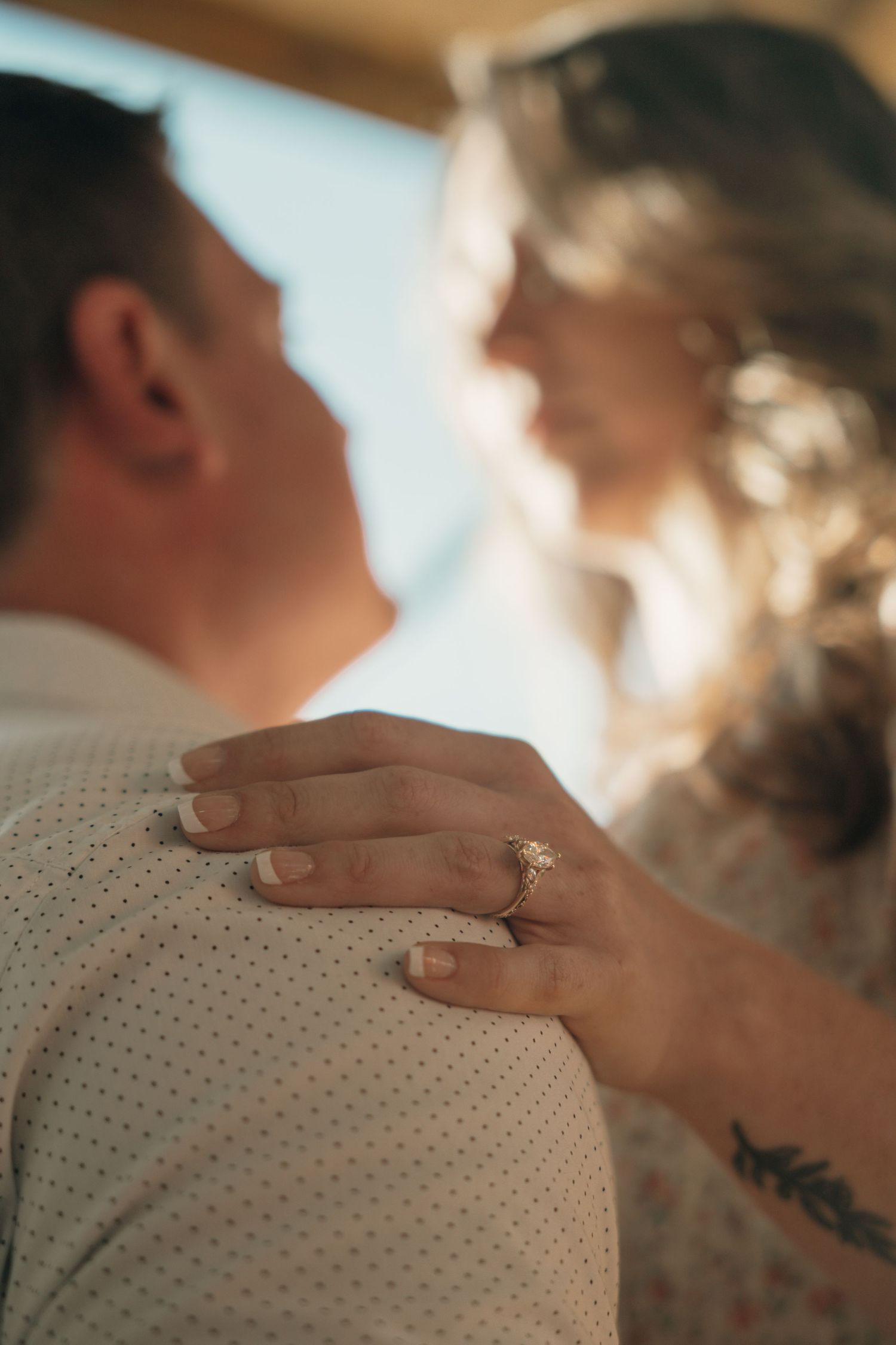 Close-up of a woman's hand with an engagement ring resting on a man's shoulder.