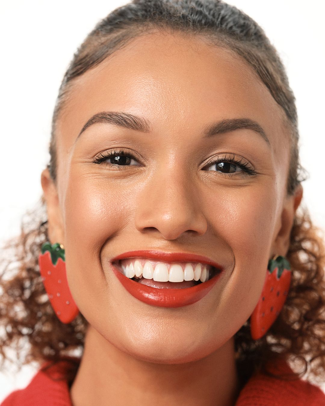 Woman smiling with red lips and strawberry earrings wearing red sweater.
