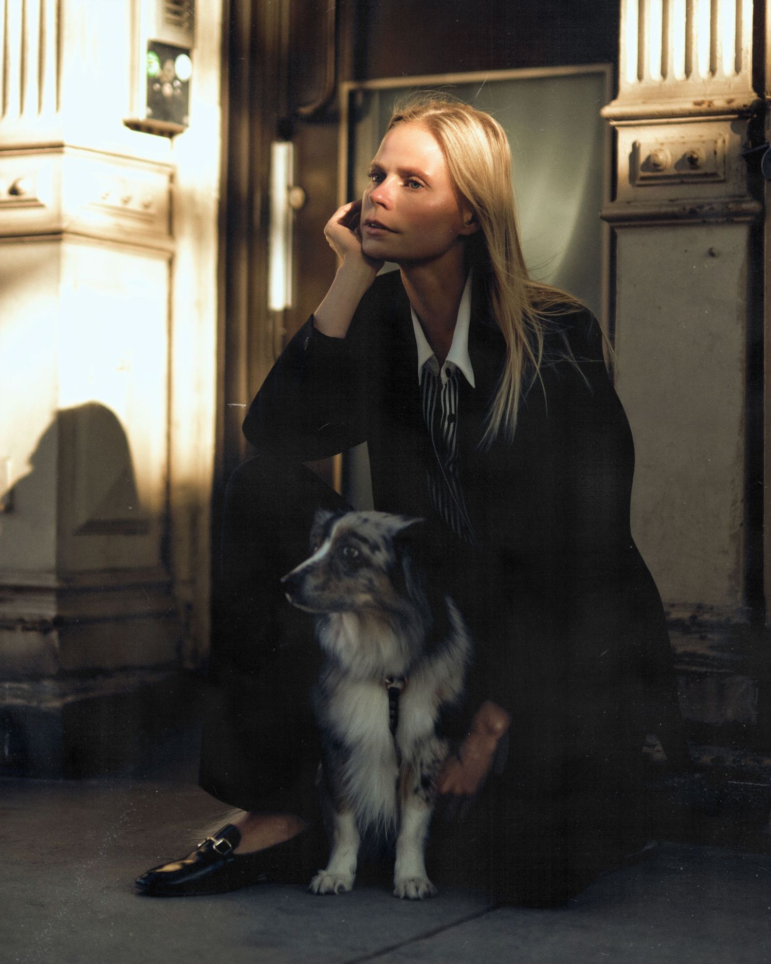 Woman in pinstripe blazer sitting with fluffy gray and white dog on urban steps.