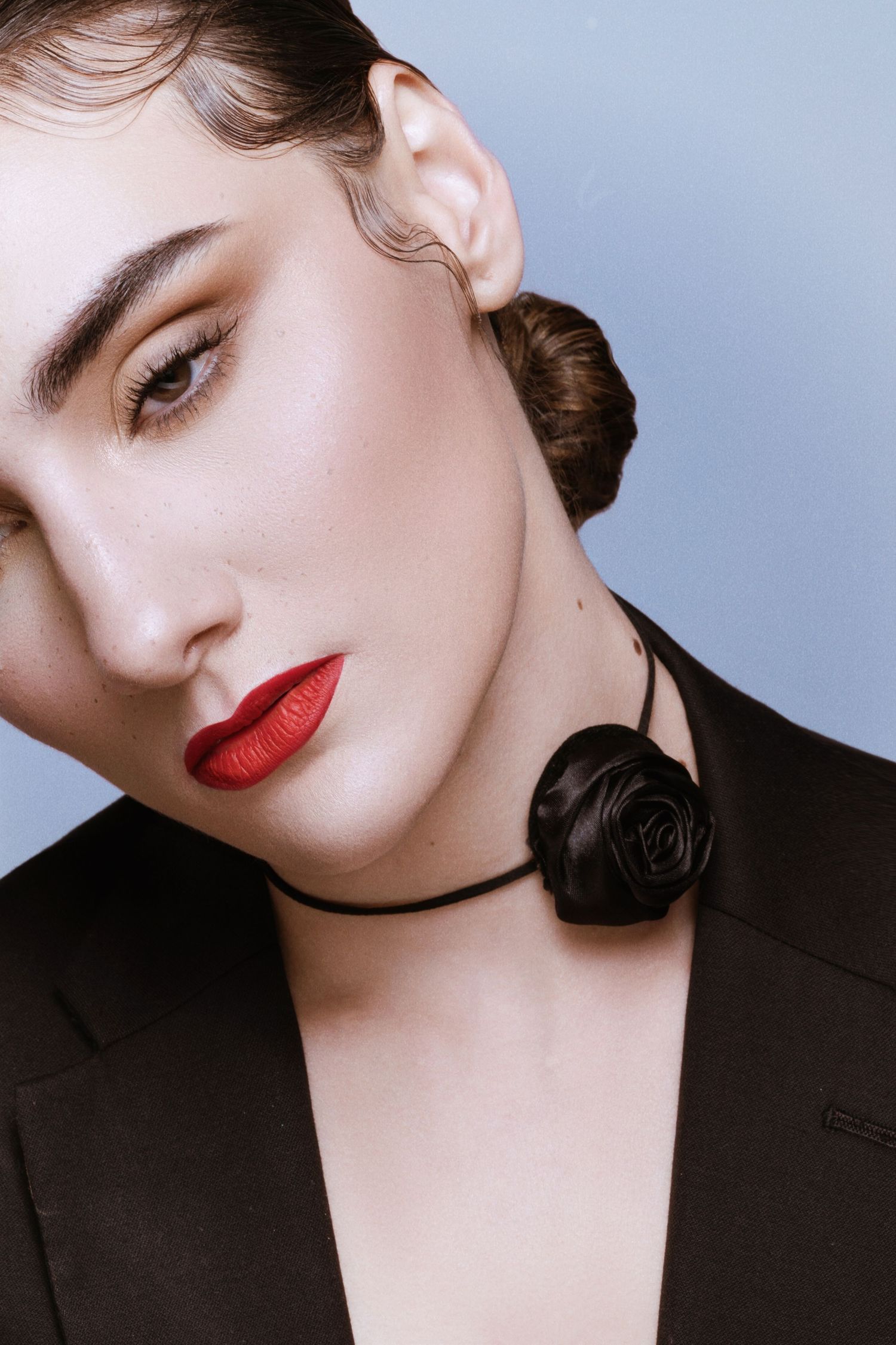 Close-up portrait of a model with red lips, wave-set hair, and a black satin rose choker necklace.