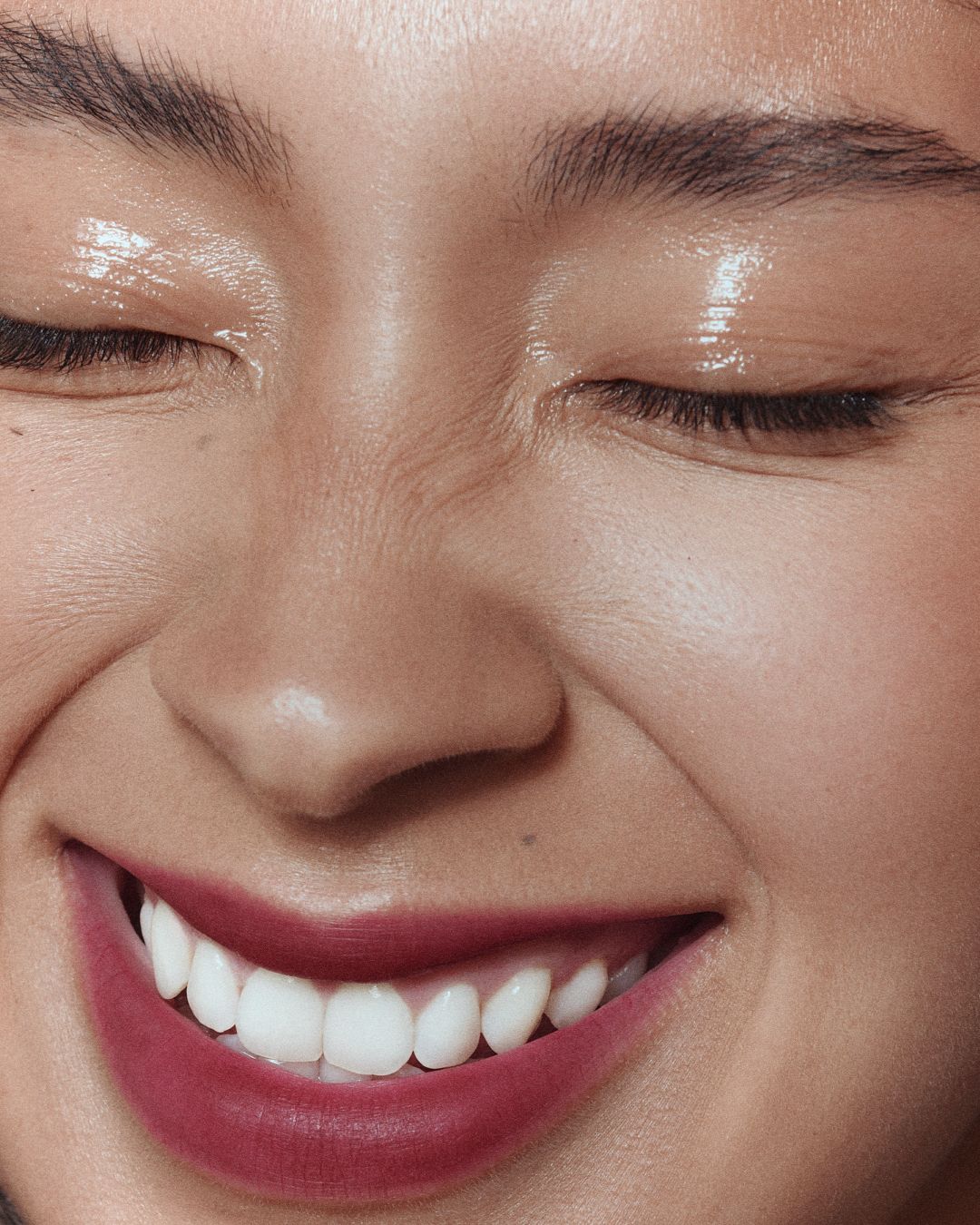 Close-up of smiling woman with glowing skin and berry lips beauty shot.