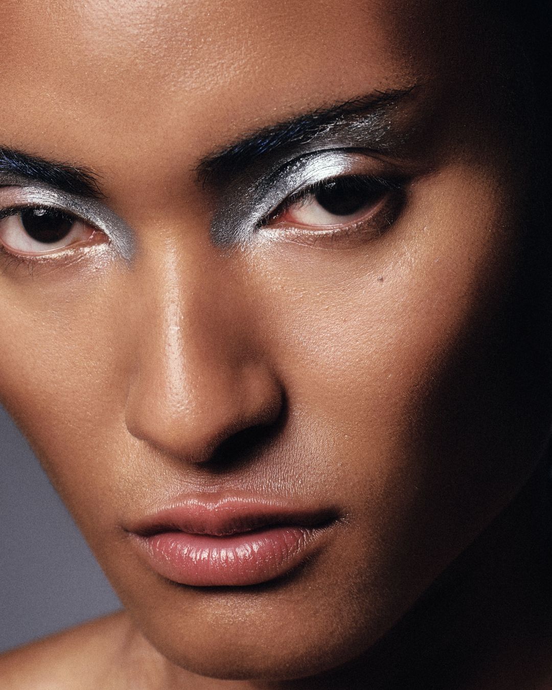 Close-up of model with dramatic silver metallic eye makeup against dark background.