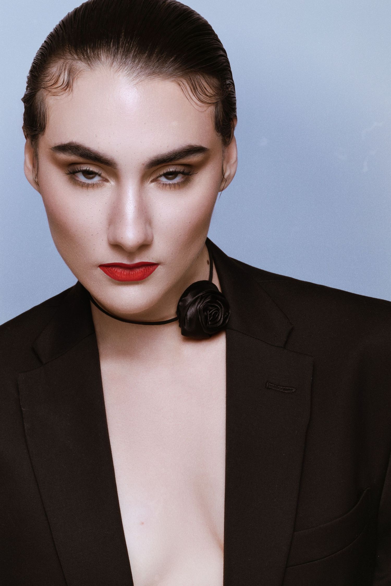 Fashion portrait of a model in a black blazer with red lips and dramatic eye makeup and rose choker.