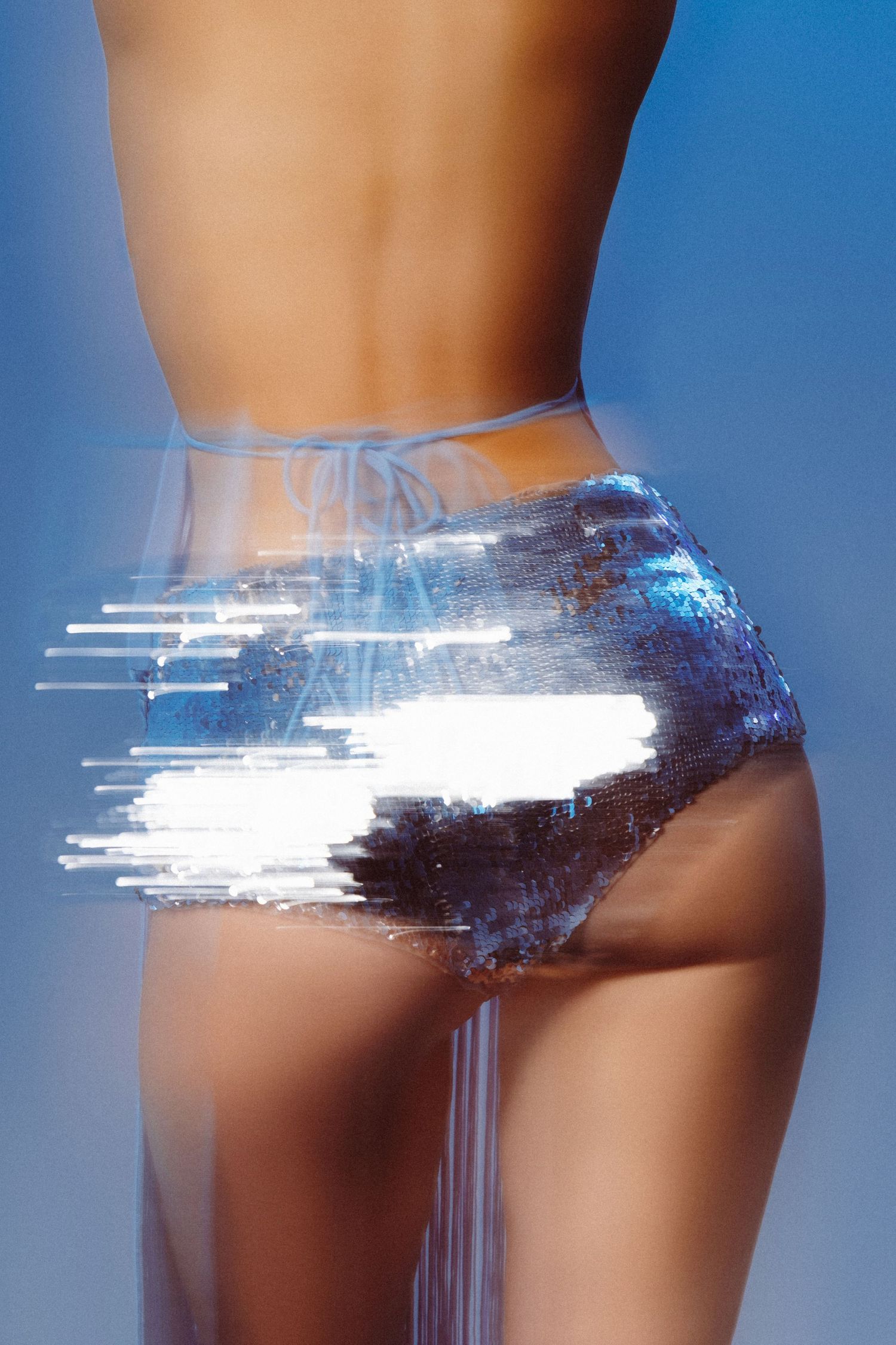 Woman in shimmering blue sequin shorts with glitch light effect against blue background.