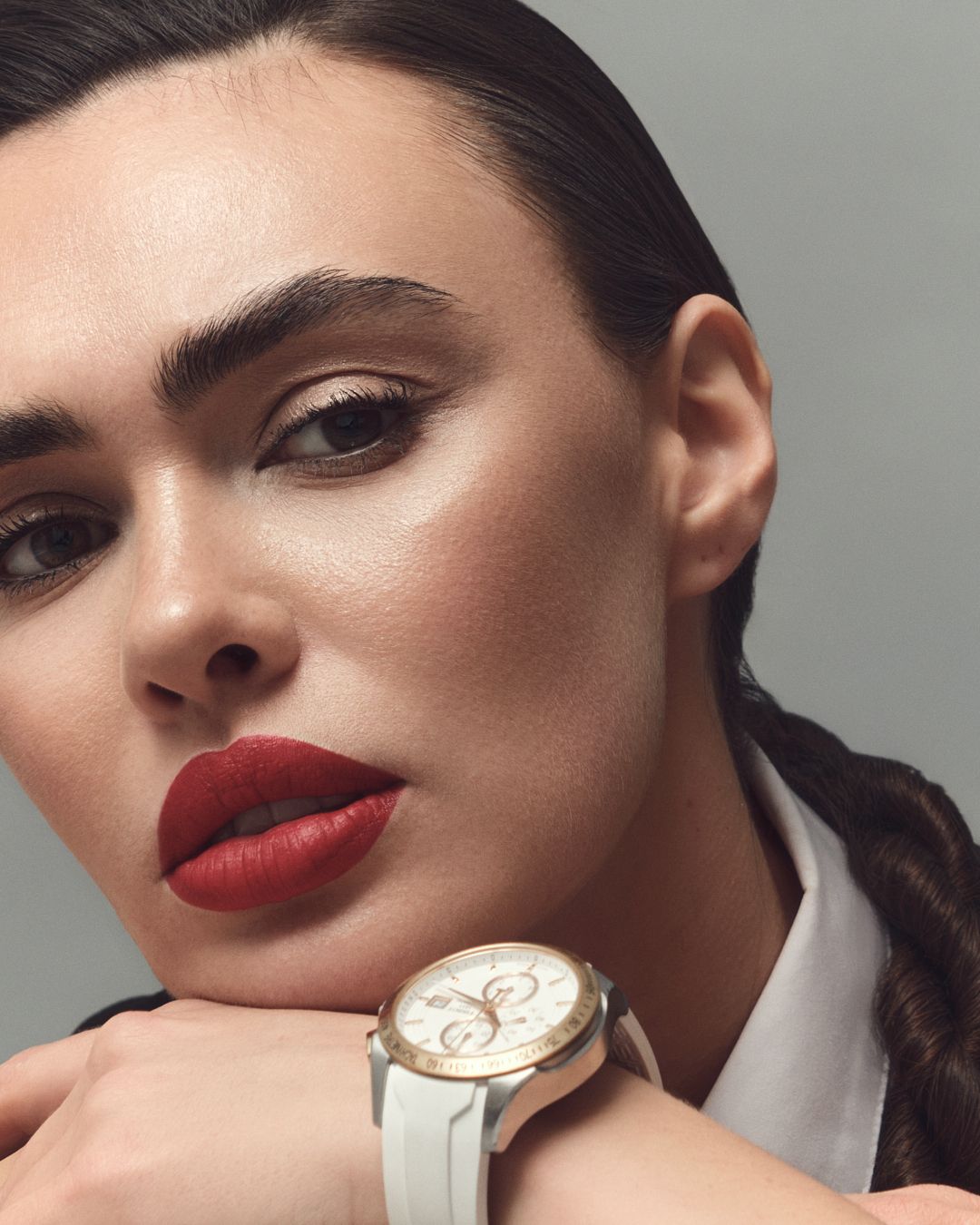 Close-up of a woman with red lips and sleek hair posing with a white and rose gold luxury watch on her wrist.