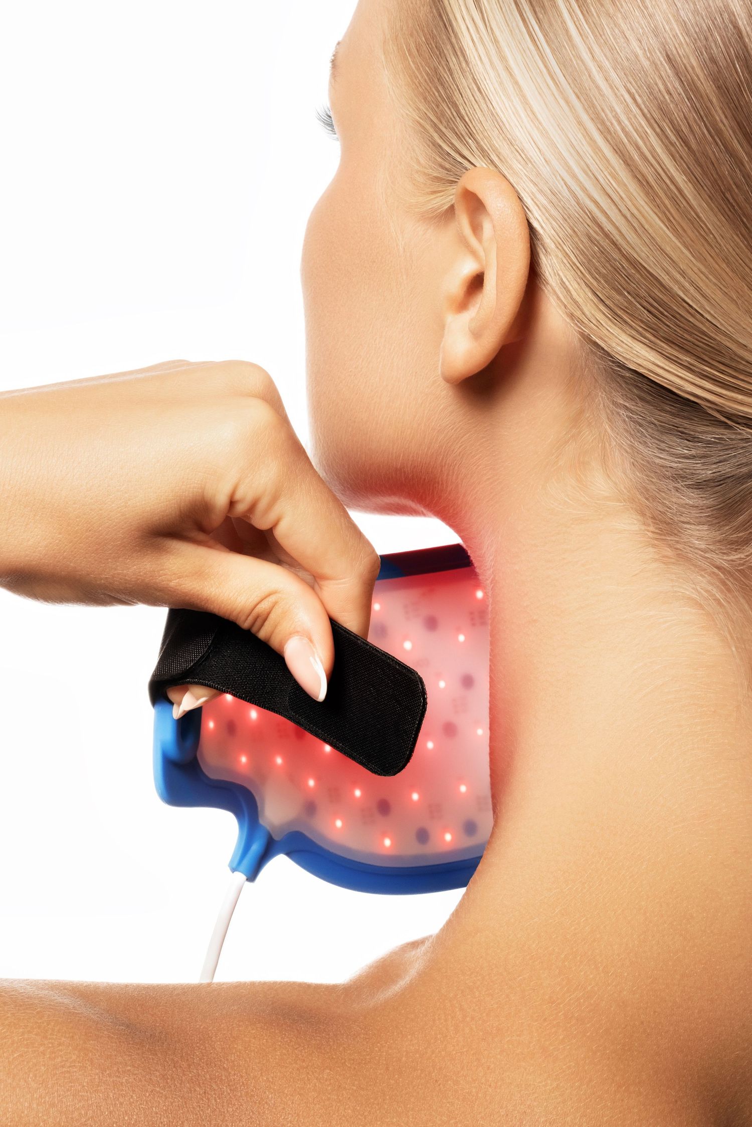 Woman applying red light therapy device to neck against white background.