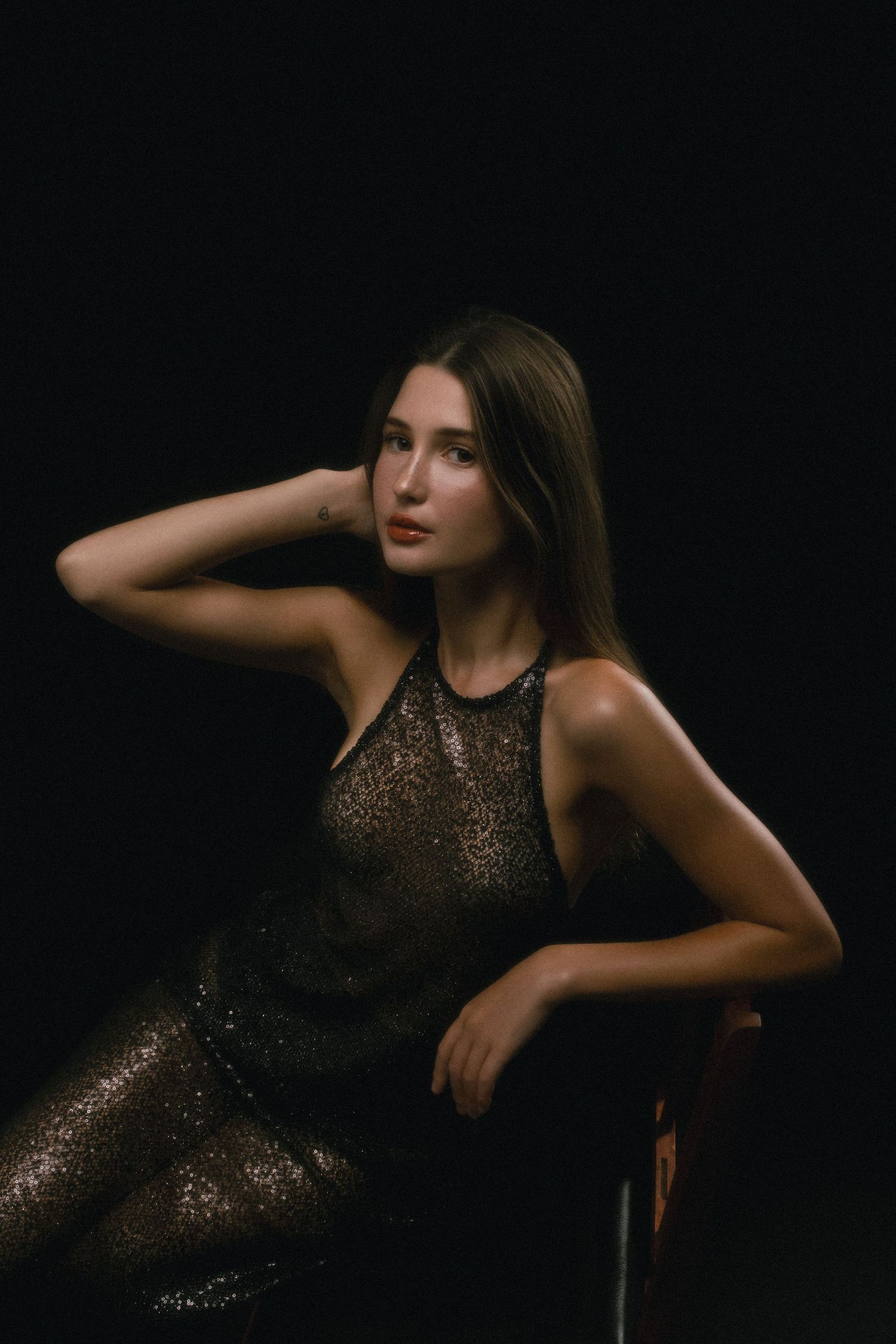 Woman in black sequin dress seated against dark background, elegant studio portrait photography.