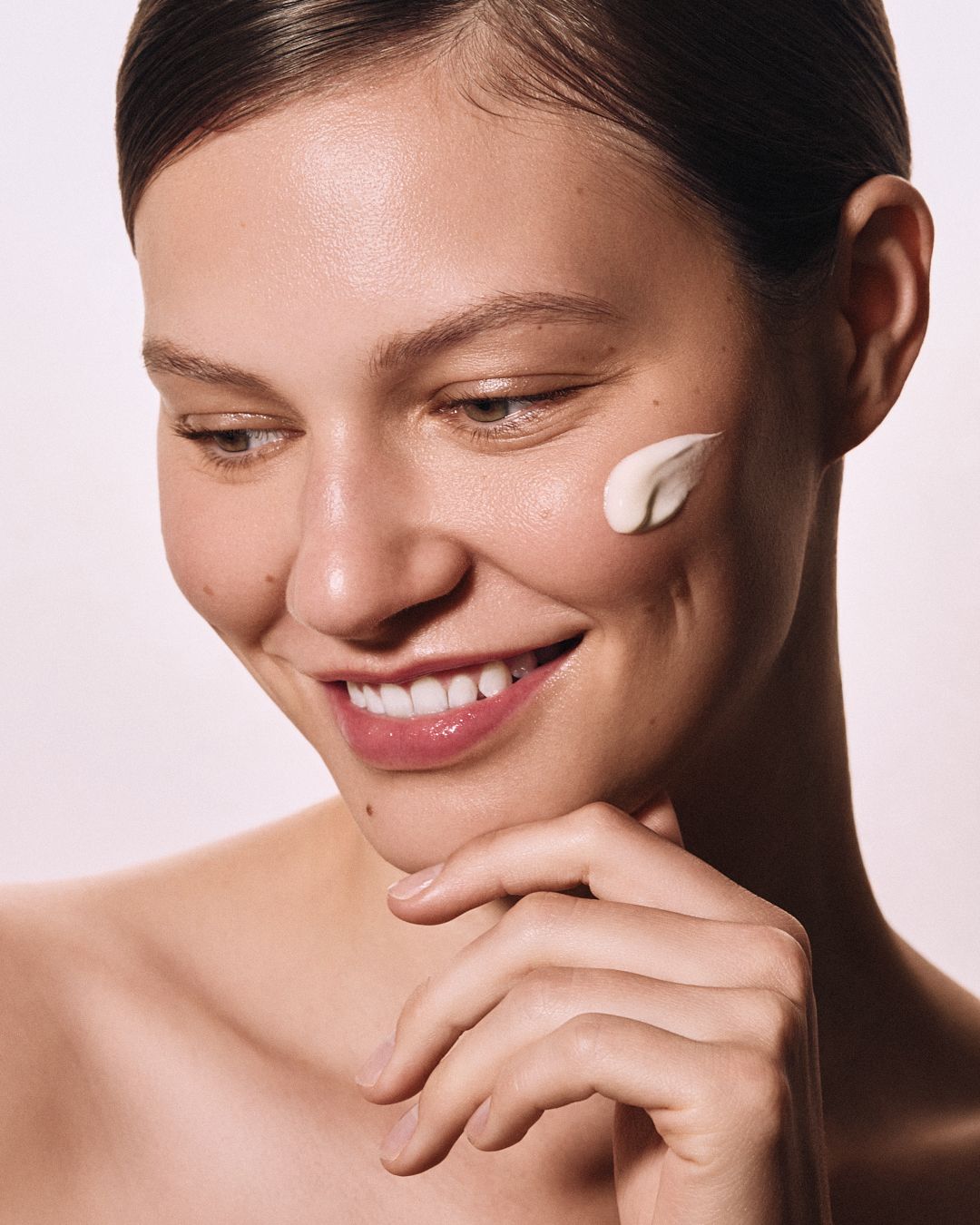 Smiling woman with cream on cheek showcasing skincare product application.