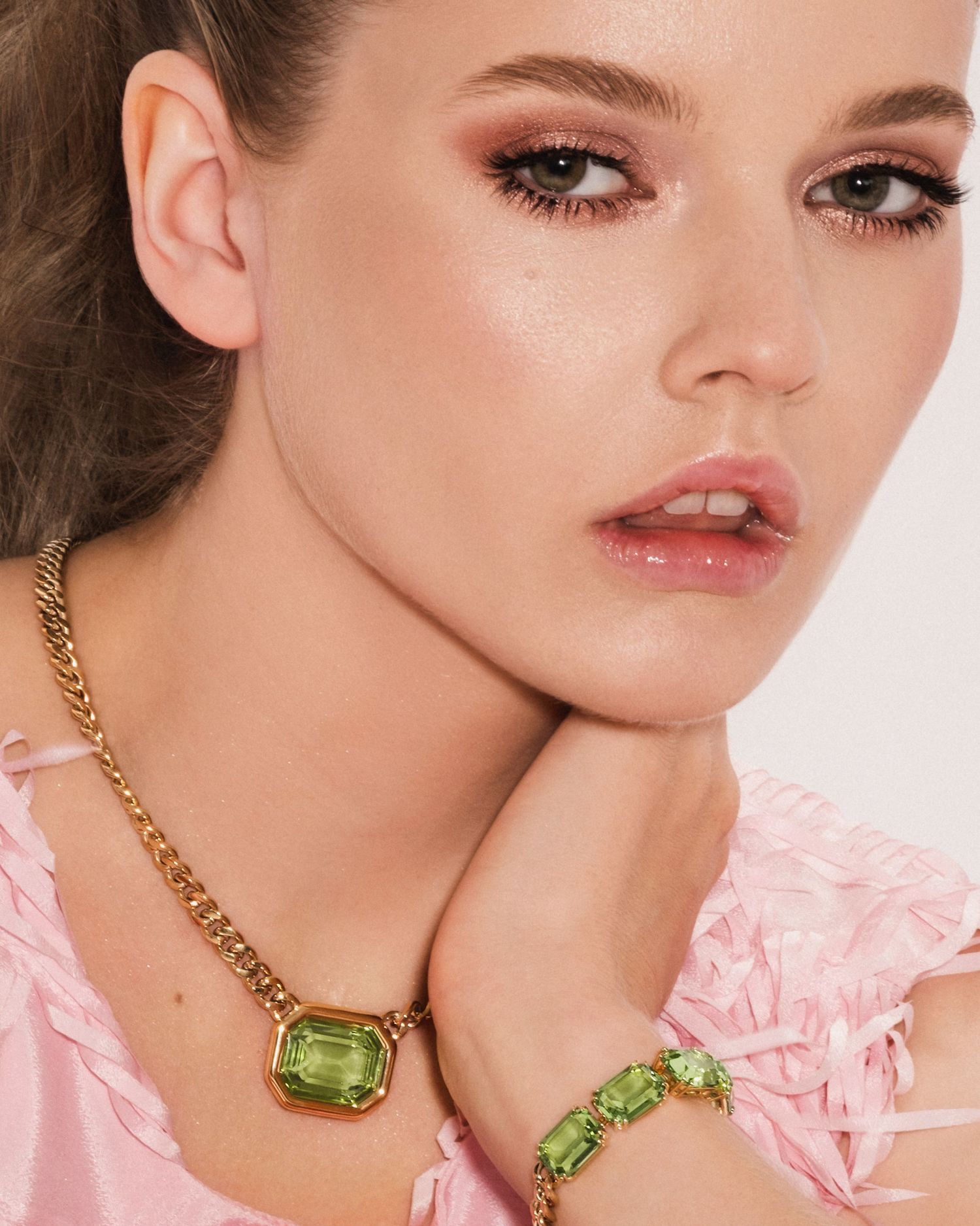 Model wearing gold chain necklace with green peridot pendant and matching bracelet, styled with pink ruffled top.