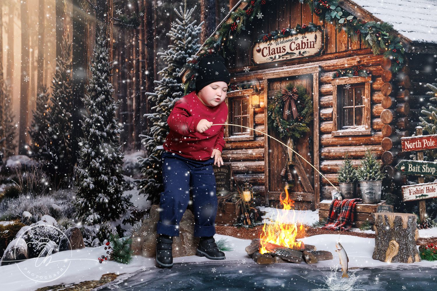 Young boy in red sweater plays near a snowy log cabin Christmas scene with a campfire and falling snow.
