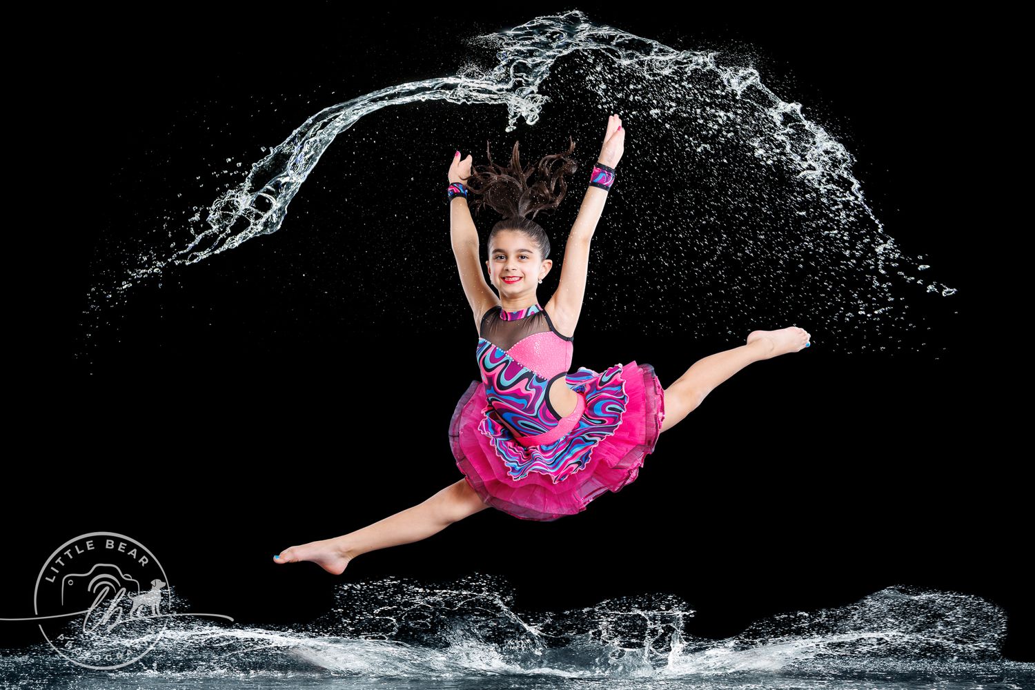 Young dancer leaps in pink tutu costume with dramatic water splash effect.