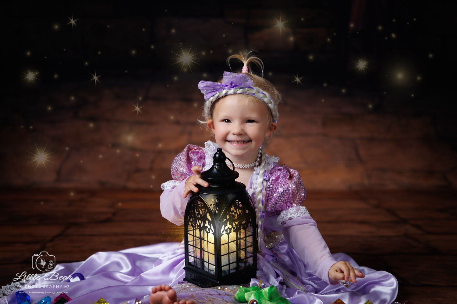 Smiling toddler girl in Rapunzel princess costume holding a glowing lantern with magical sparkles in background.