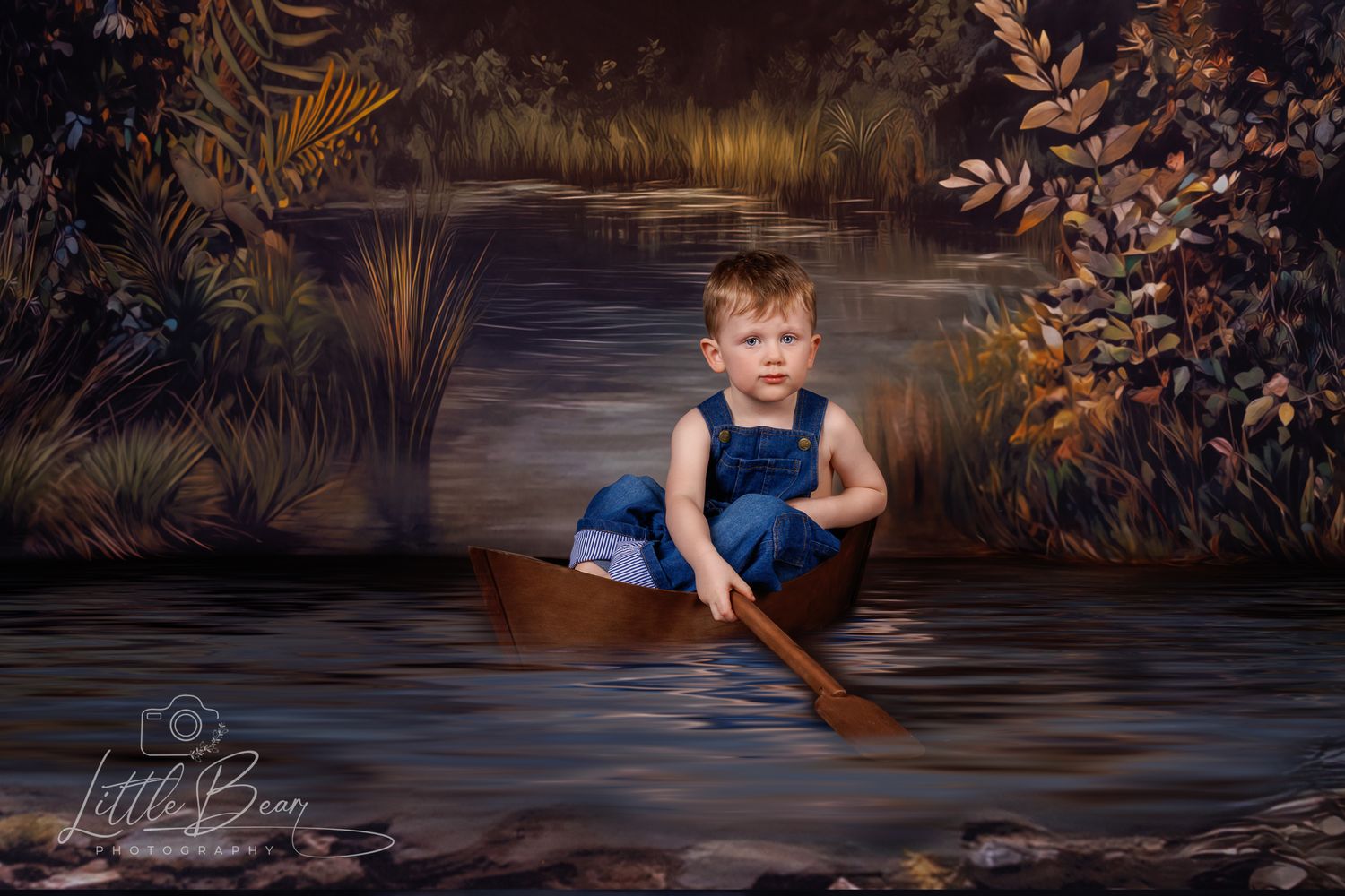 Young boy in denim overalls rowing a wooden boat through a magical forest stream with autumn leaves.