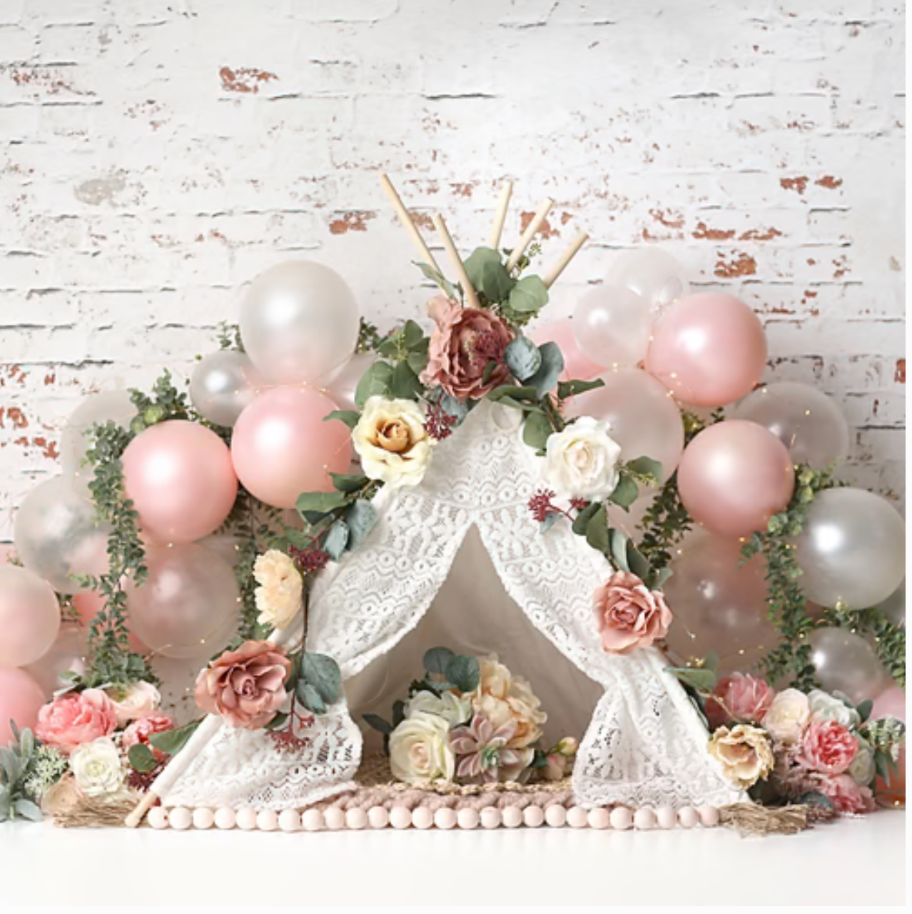 Pink floral boho teepee cake smash backdrop with balloons and roses on a white brick background.