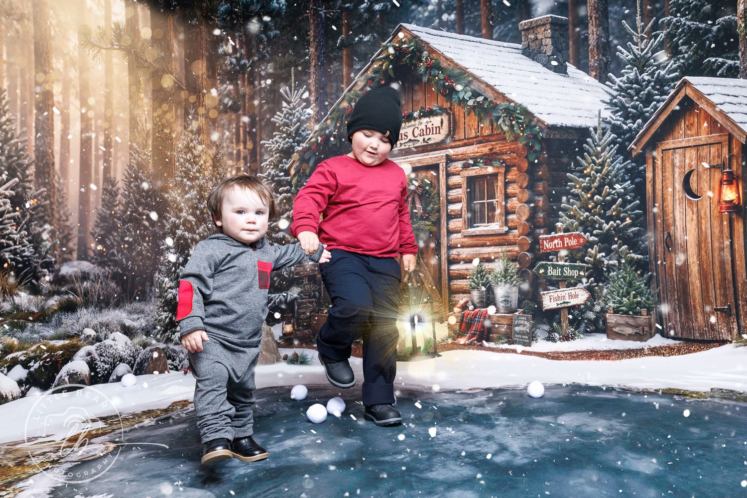 Two young children playing in snow near festive log cabins with holiday decorations in a winter wonderland scene.