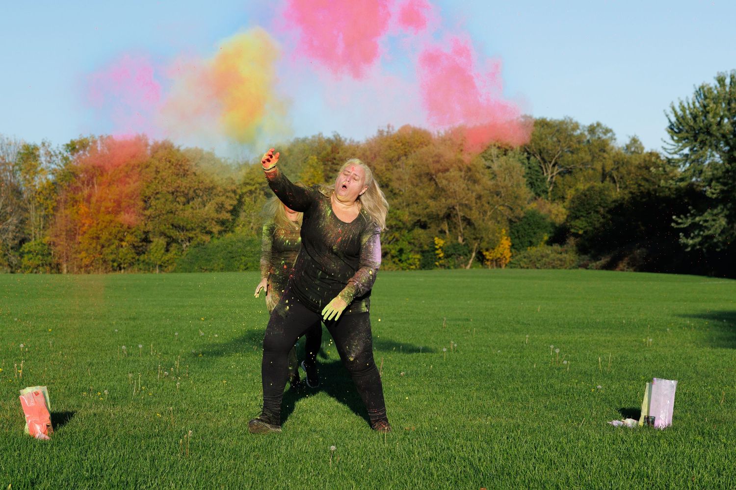 Person throwing colorful pink and yellow powder in the air on a sunny green field.