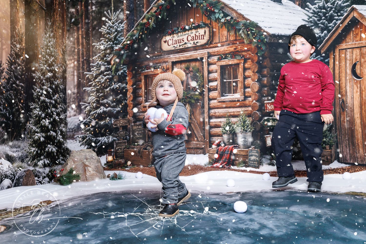 Two young boys playing in snow near a festive log cabin with Christmas trees in a winter holiday scene.