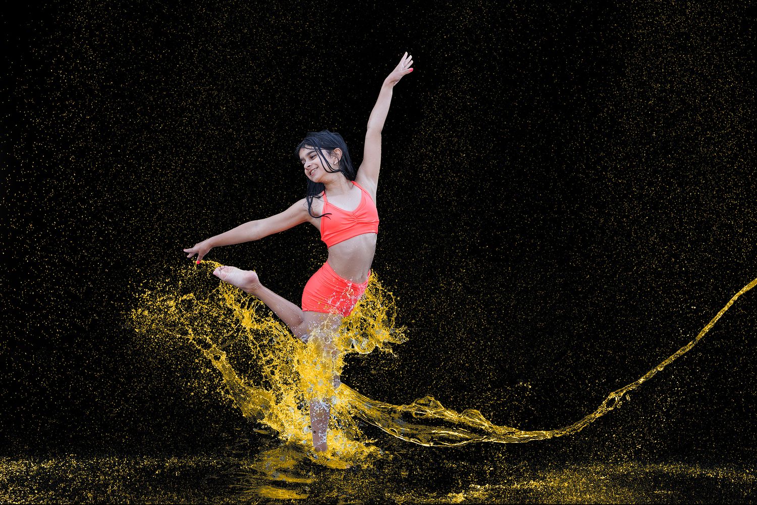 A dancer leaps gracefully through golden yellow liquid splashes against a dark background, wearing a bright coral athletic outfit.