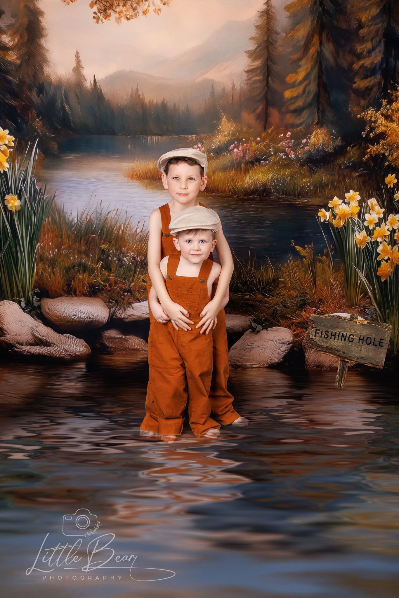 Two boys in matching rust overalls and newsboy caps posing by a painted riverside fishing hole backdrop.