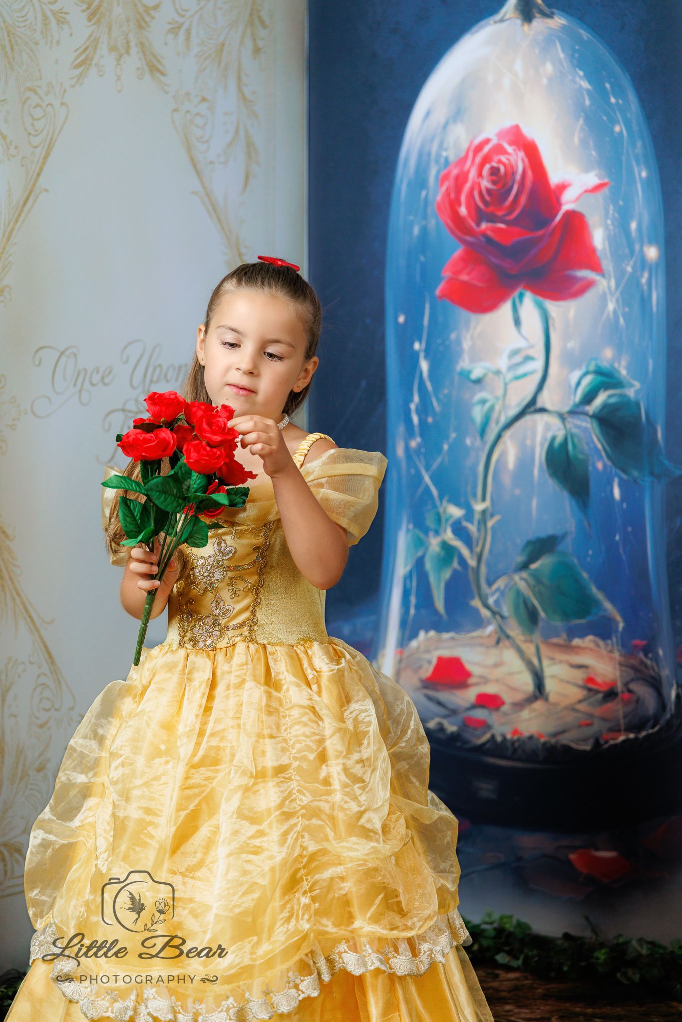 Young girl in yellow Belle gown holds red roses, Beauty and the Beast enchanted rose backdrop, Little Bear Photography.
