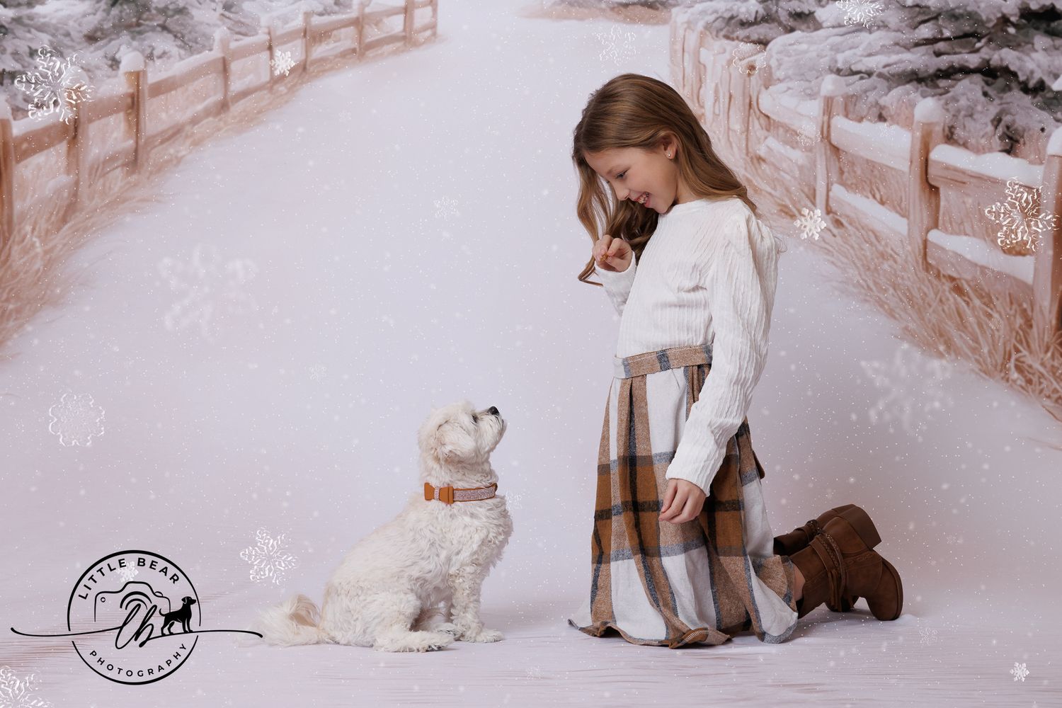 A young girl in a plaid skirt kneels in snow beside a white fluffy dog wearing an orange collar.