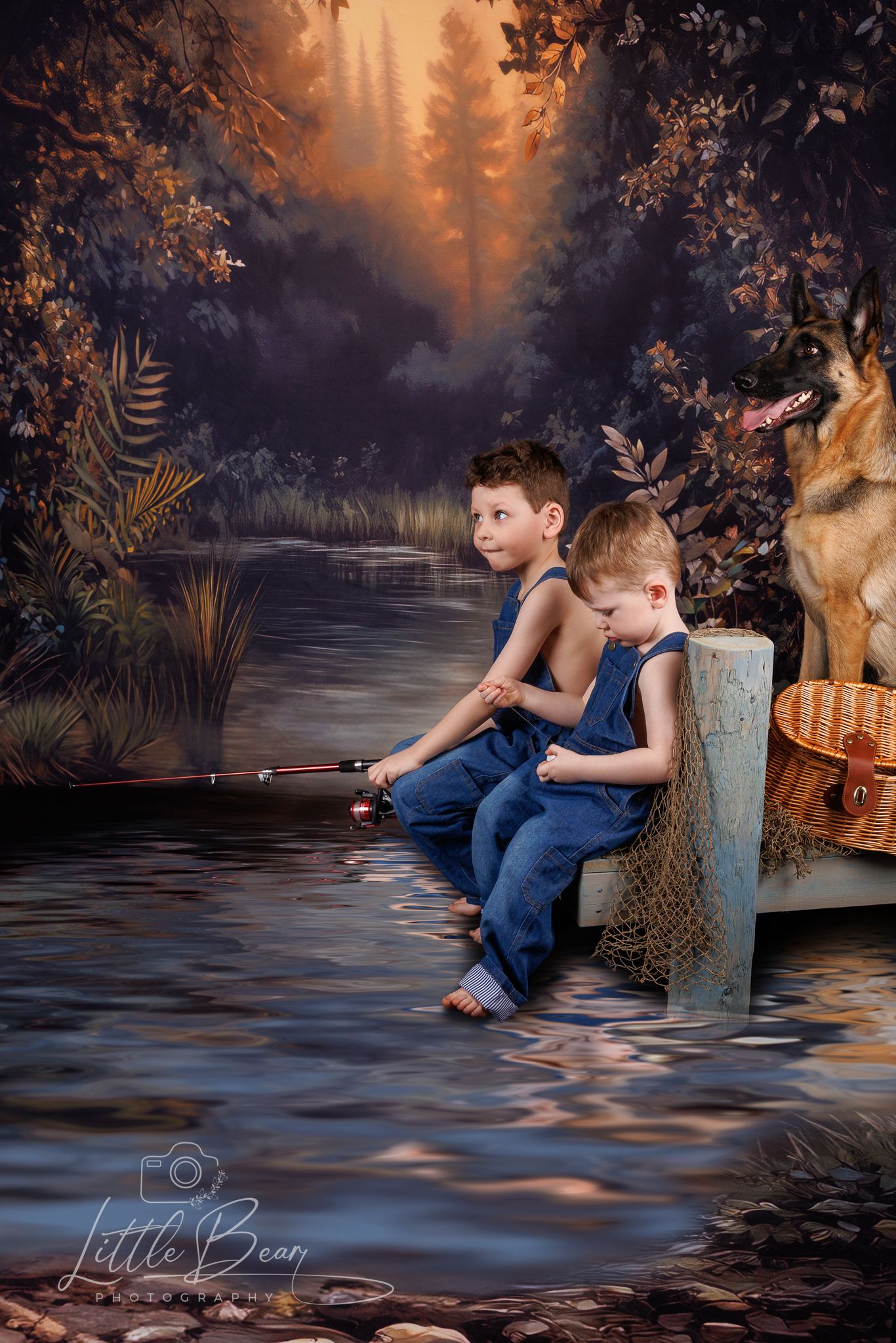 Two barefoot boys in blue overalls fishing together by a woodland stream with a German Shepherd nearby.