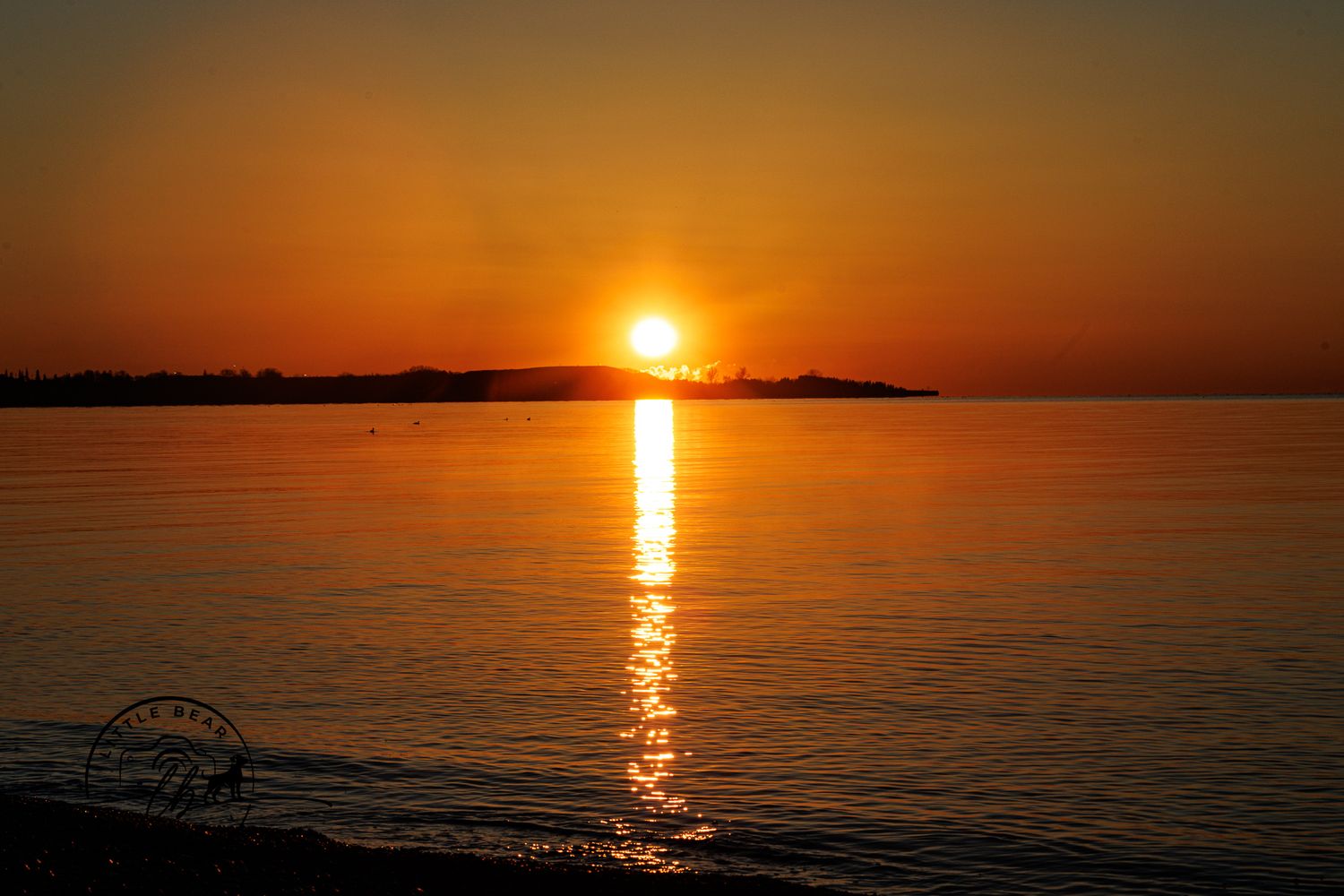 Stunning golden sunset reflecting over calm ocean water with silhouetted shoreline on the horizon.