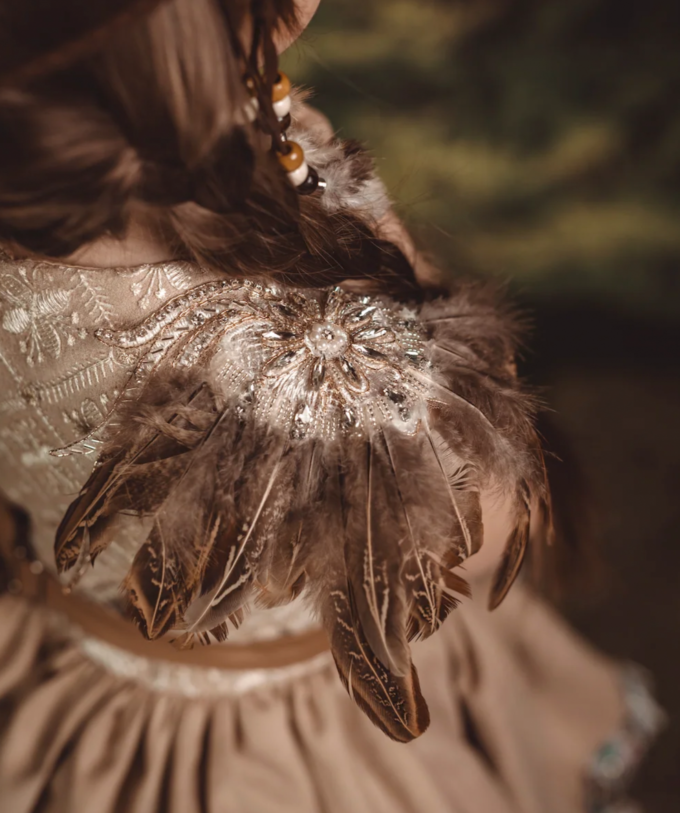 Close-up of an ornate feathered brooch with beaded embellishments on a beige embroidered dress.