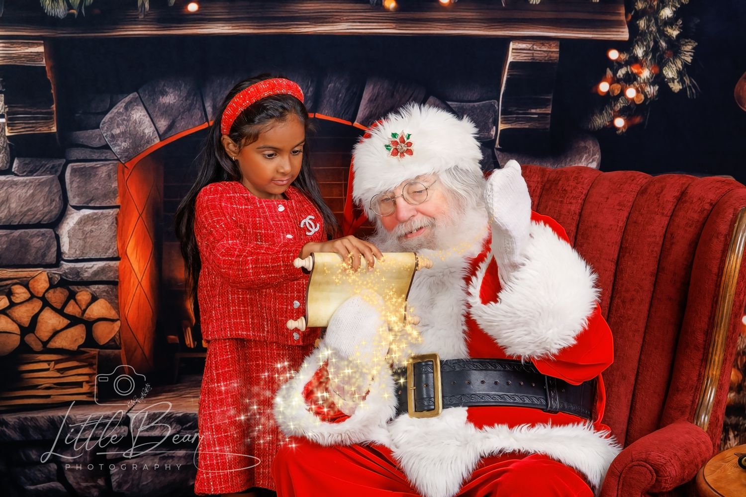 A young girl in red pajamas opens a magical gift box with Santa Claus by a decorated fireplace.