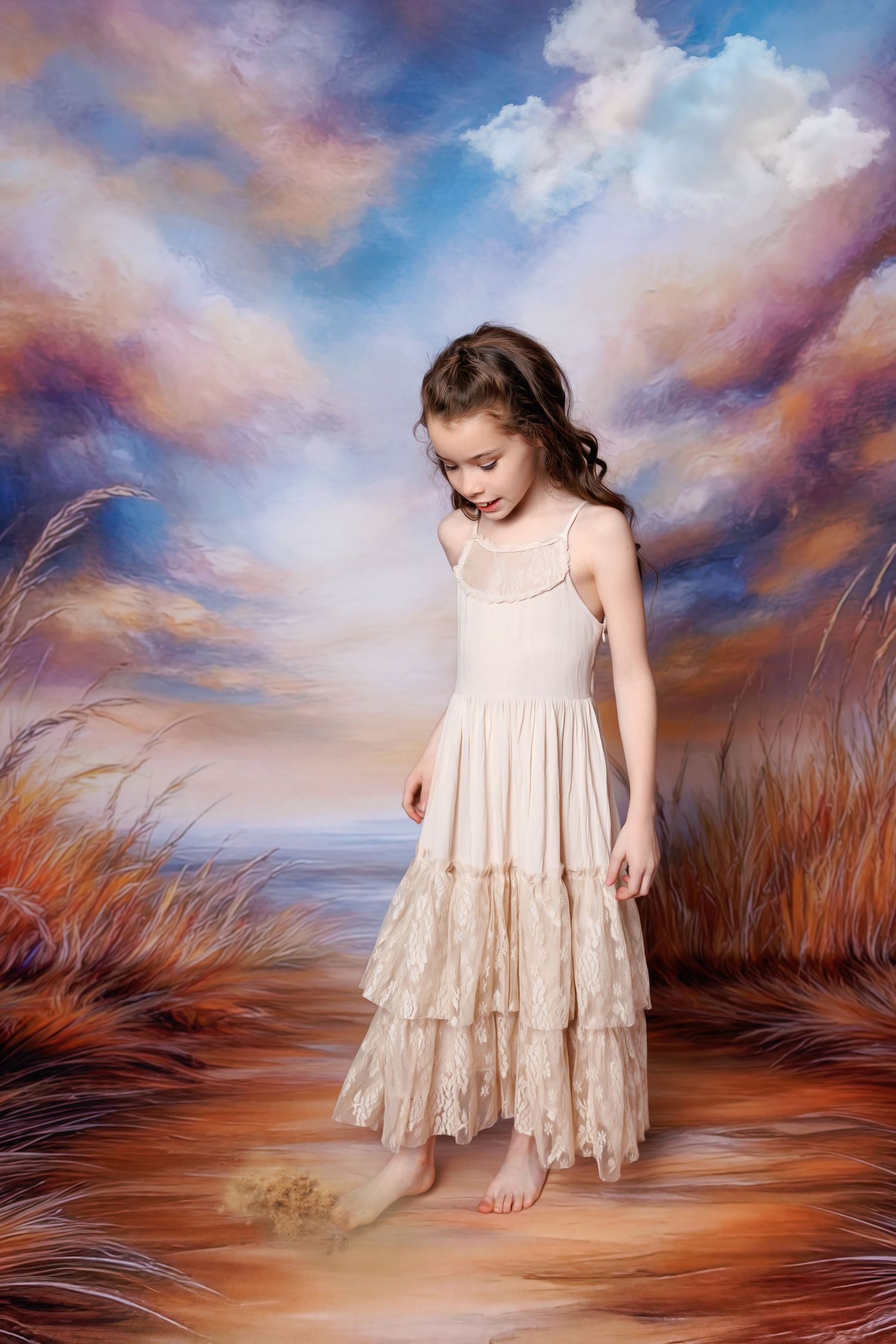 A barefoot girl in a cream lace dress looks down while standing before a dramatic painted sky backdrop.