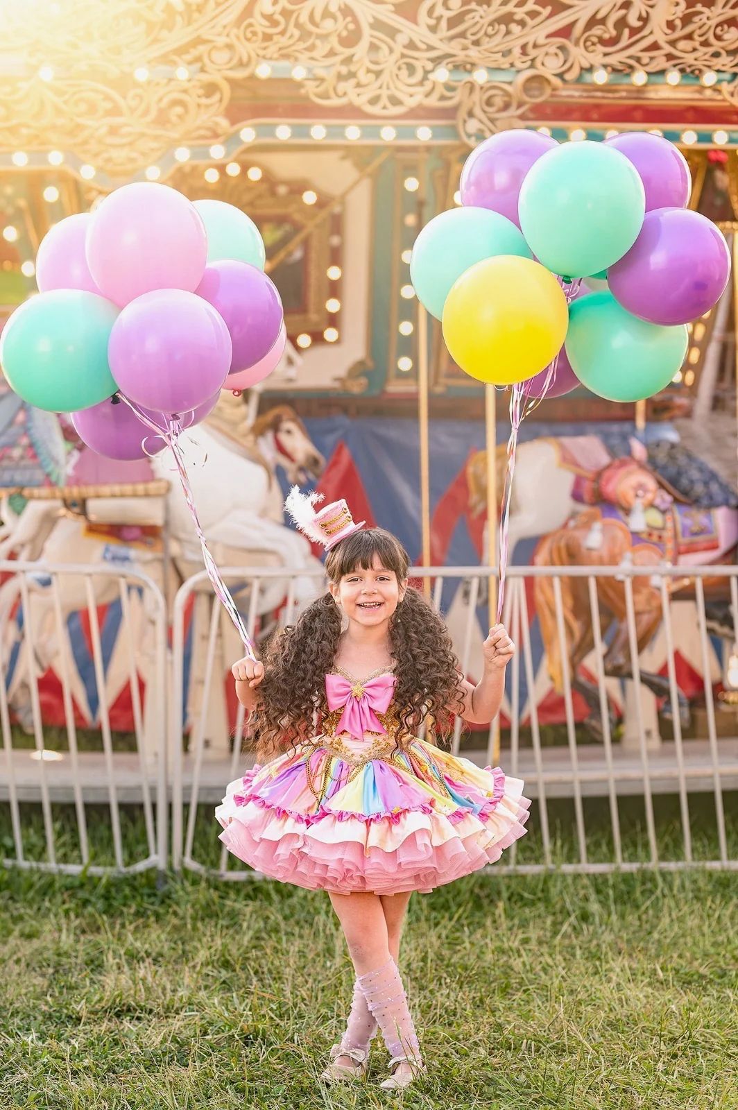 Young girl in colorful ruffled dress holds pastel balloons at carnival carousel.