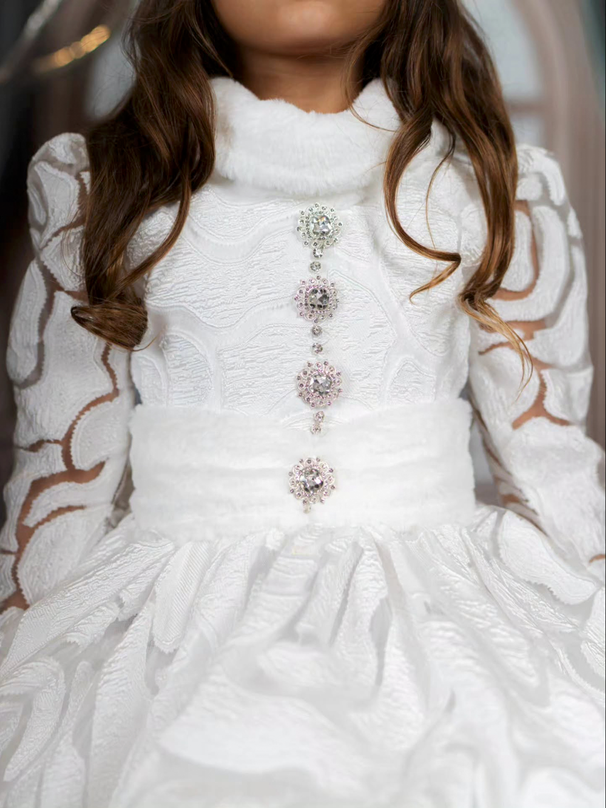 Girl in white lace long-sleeve dress with rhinestone brooch embellishments down the front bodice.