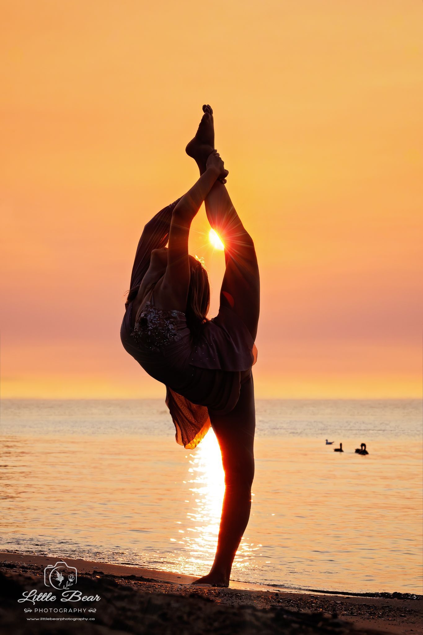 Silhouette of a person performing a standing split yoga pose on a beach at sunset with golden sky.