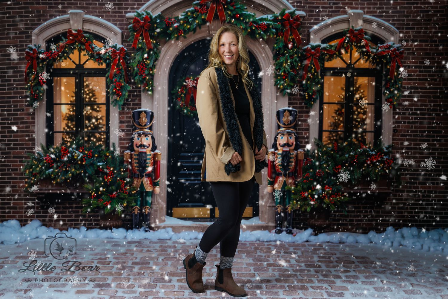 Woman posing in front of Christmas-decorated brick building with nutcrackers and garlands in falling snow.