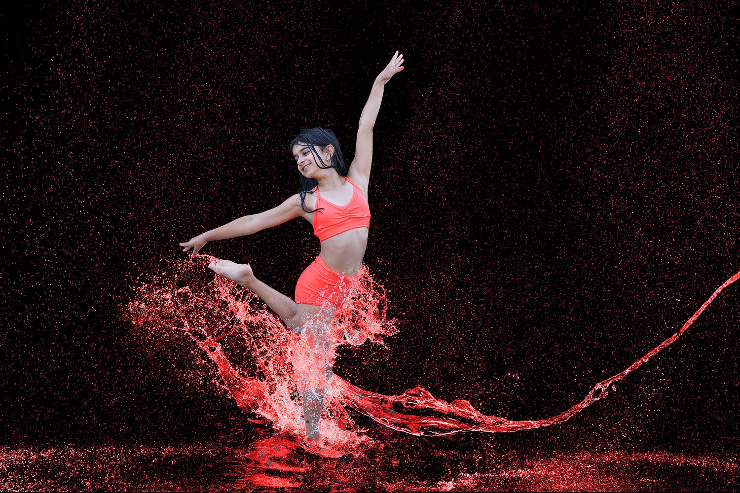 A dancer in red activewear leaps gracefully amid dramatic water splashes against a dark background.