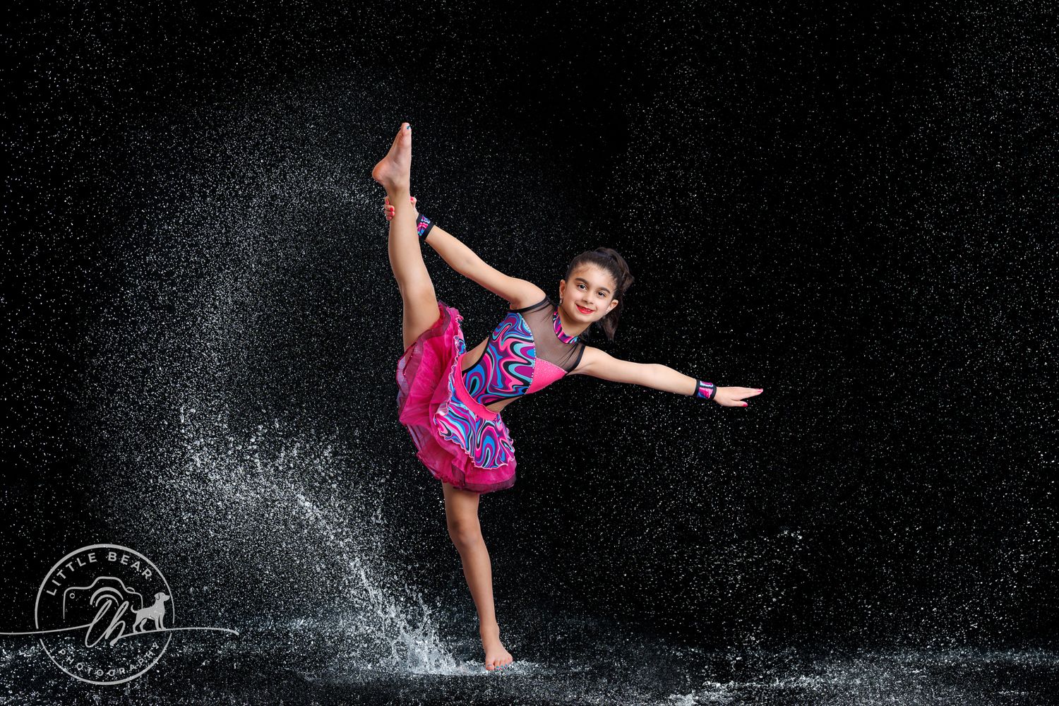 Young dancer performs high leg extension pose with dramatic water splash effect.