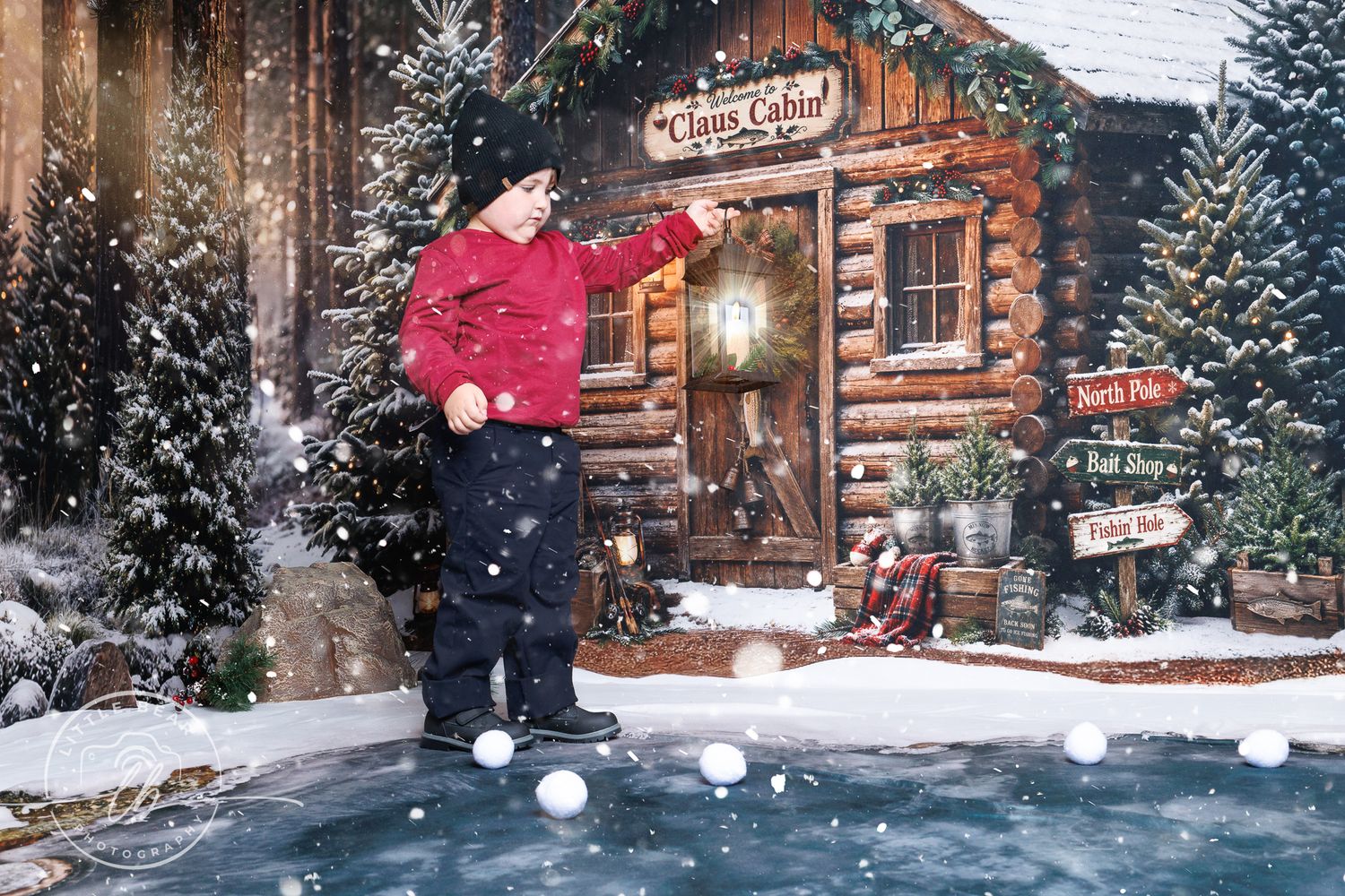 A young child in a red jacket plays in snow outside a festive Santa's cabin with Christmas trees and holiday signs.