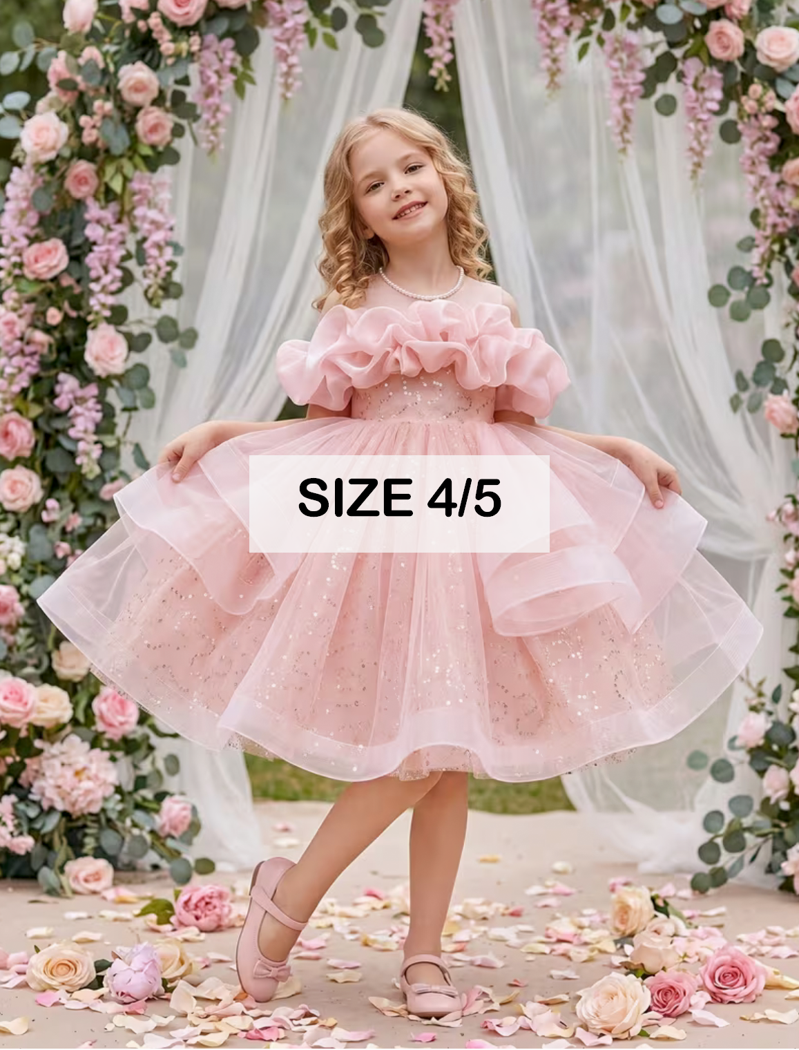 Girl wearing a pink layered tulle flower girl dress with puff sleeves, size 4/5, posed in a floral garden setting.