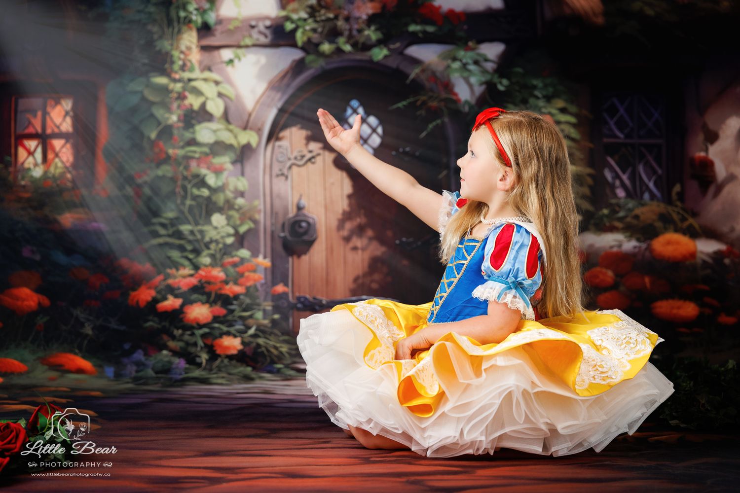 Girl in Snow White costume reaching up in a magical garden setting with roses and a stone door backdrop.