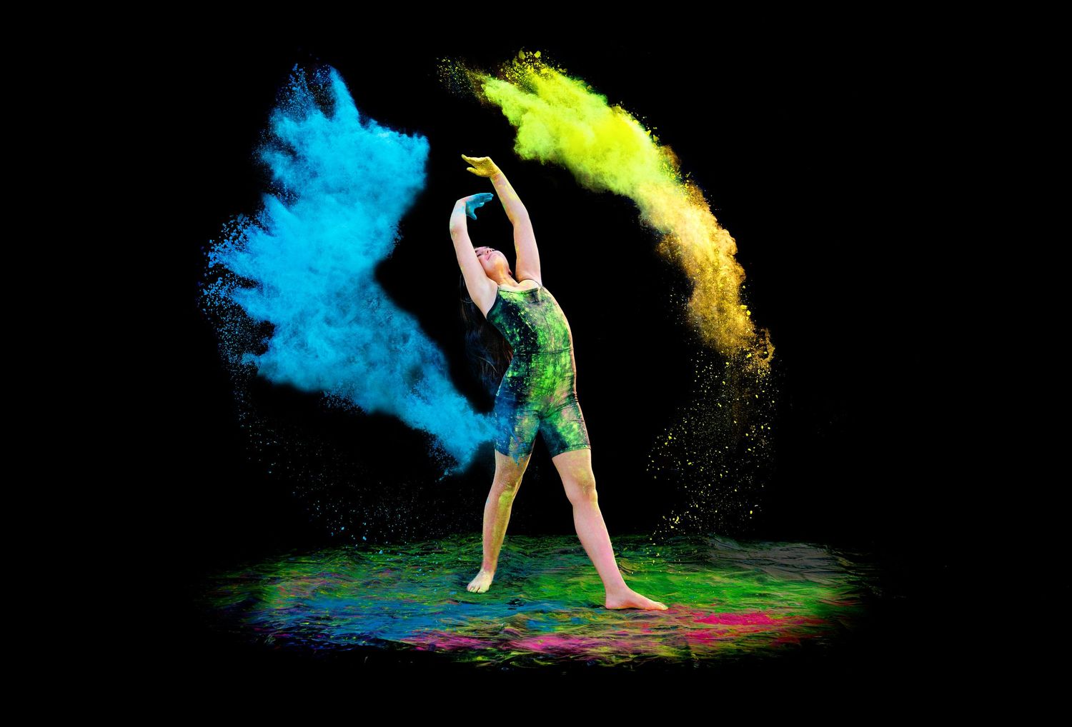 Dancer leaps dramatically surrounded by vibrant blue and yellow powder explosion on black background.