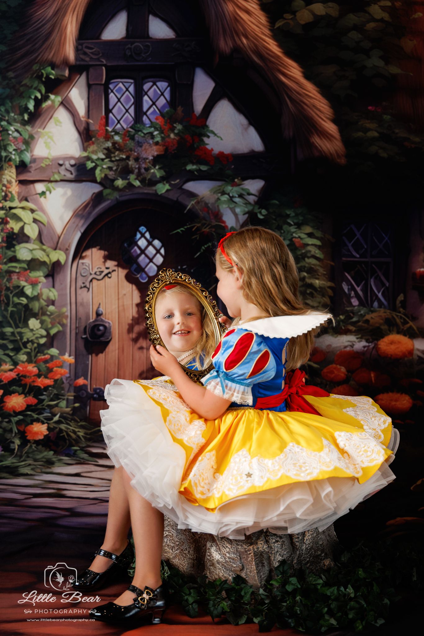 Young girl in Snow White costume holds a mirror in a fairy tale cottage photo session by Little Bear Photography.