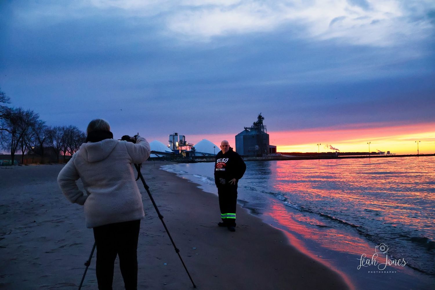 Two photographers capture a stunning sunset over Lake Michigan with a lighthouse and ship silhouetted against vibrant pink and purple skies.