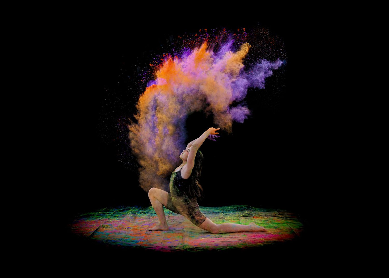 Flexible dancer performs dramatic backbend with colorful purple and orange powder cloud erupting behind them.