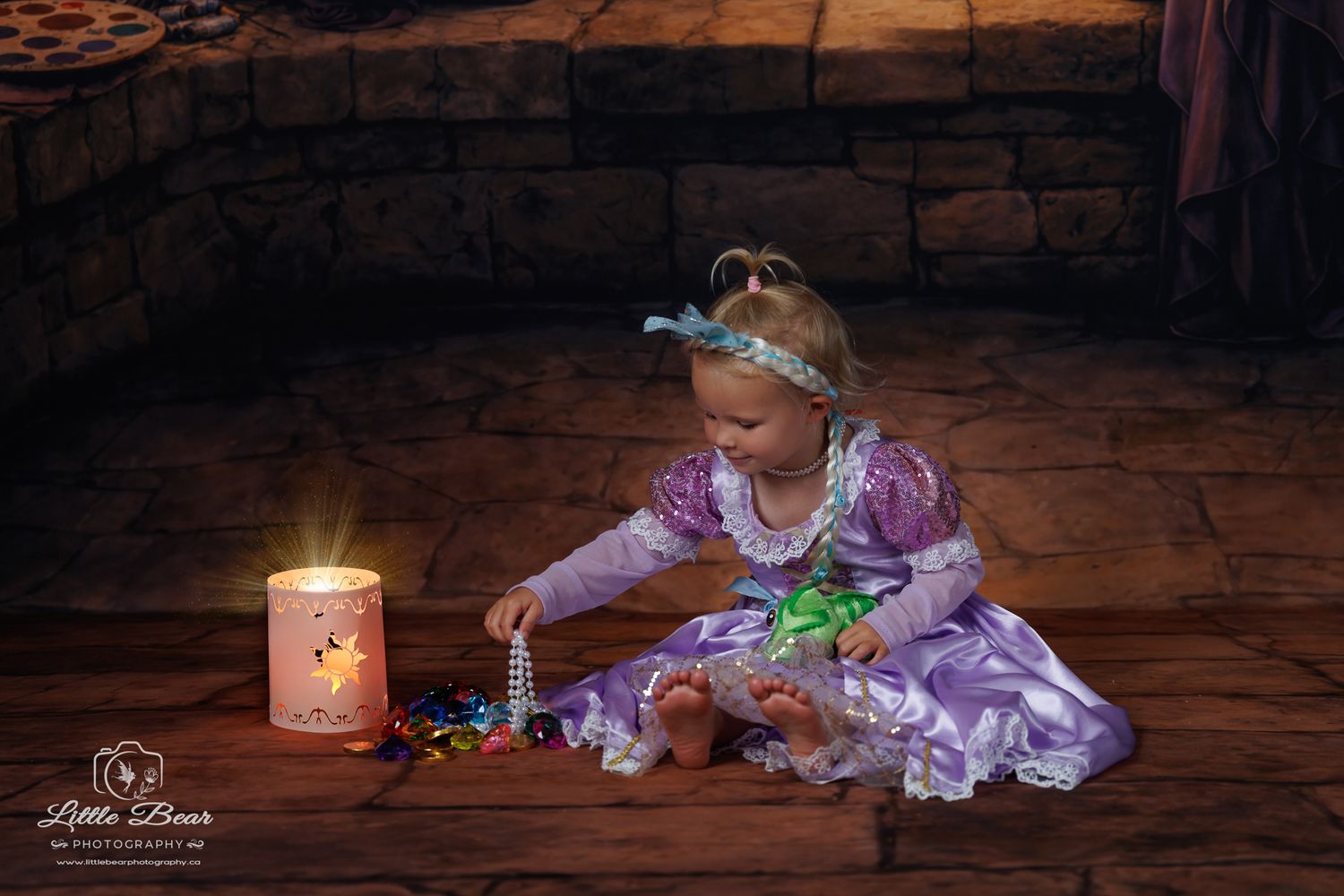 Young girl in Rapunzel costume sits on floor by glowing candle, playing with colorful beads in fairy tale setting.