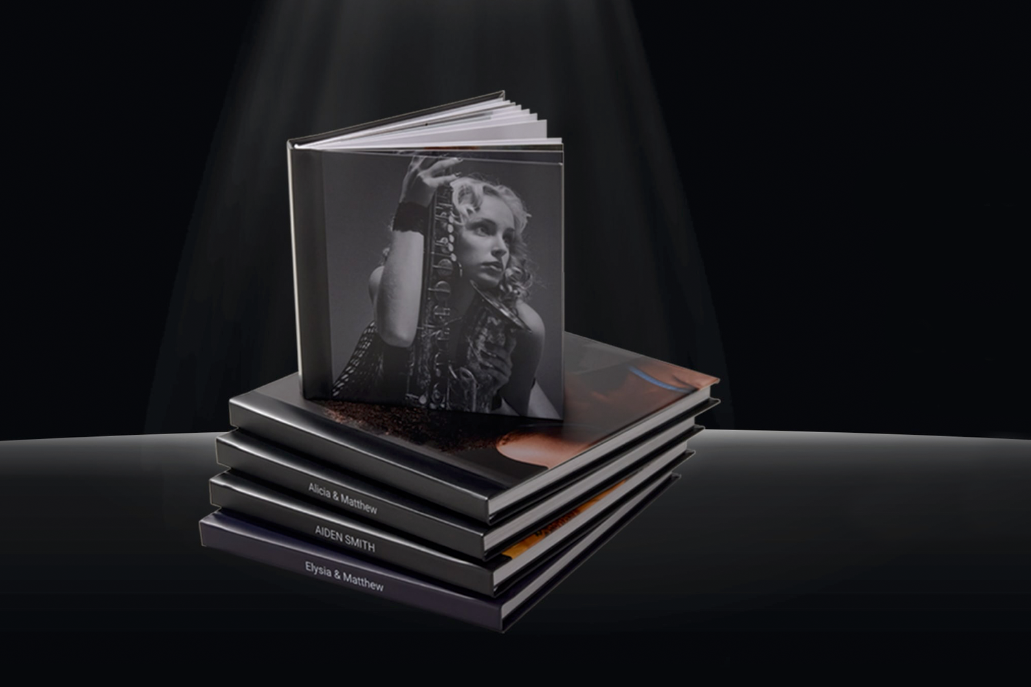 Stack of professional hardcover photo books displayed under dramatic spotlight on dark background.