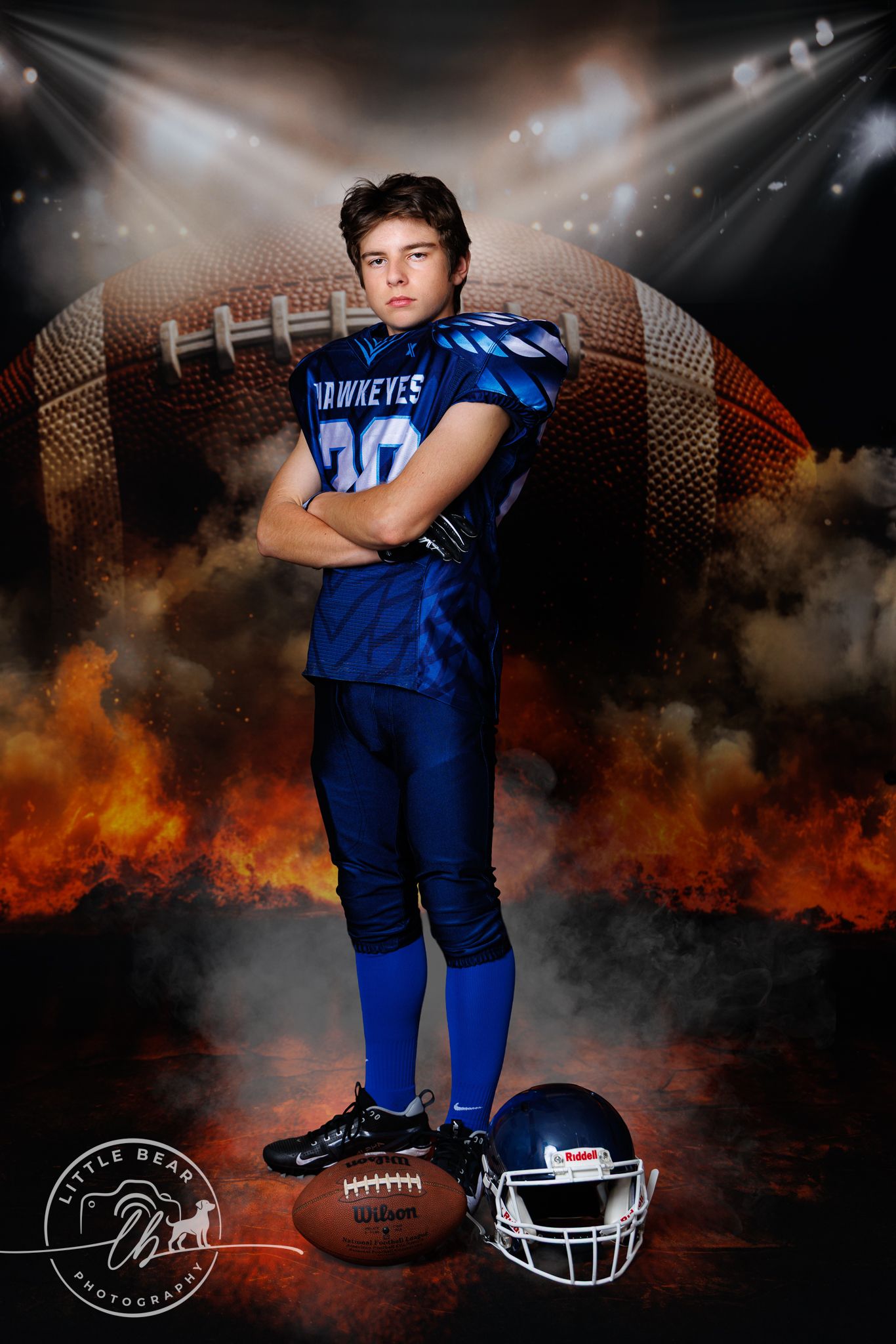Youth Hawkeyes football player number 20 standing arms crossed with fire and stadium lights background.