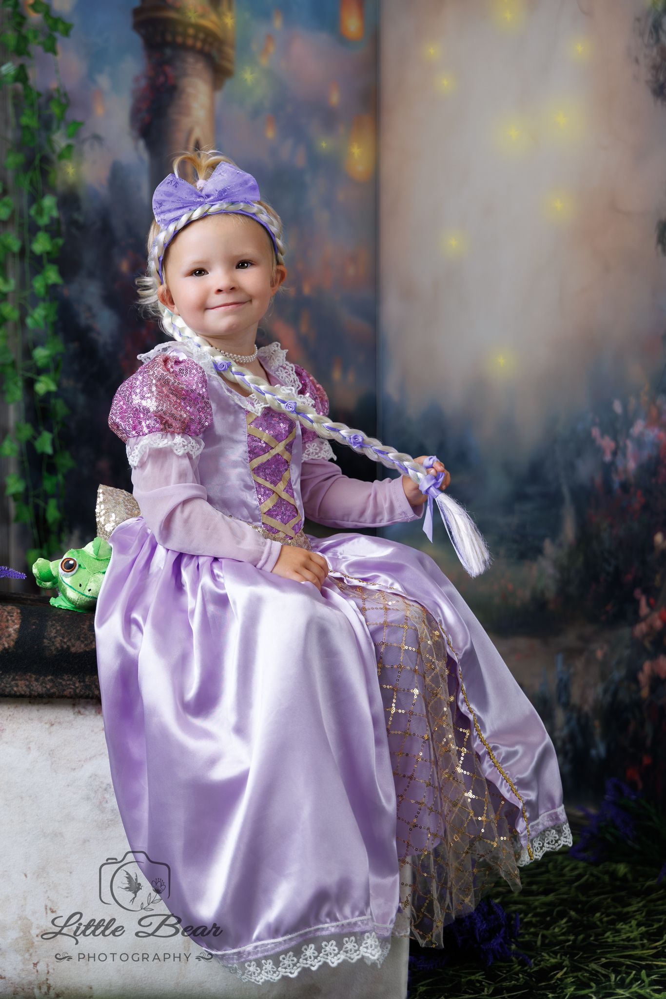 Young girl in purple Rapunzel princess costume with long braid and bow headband, seated for professional portrait photo.