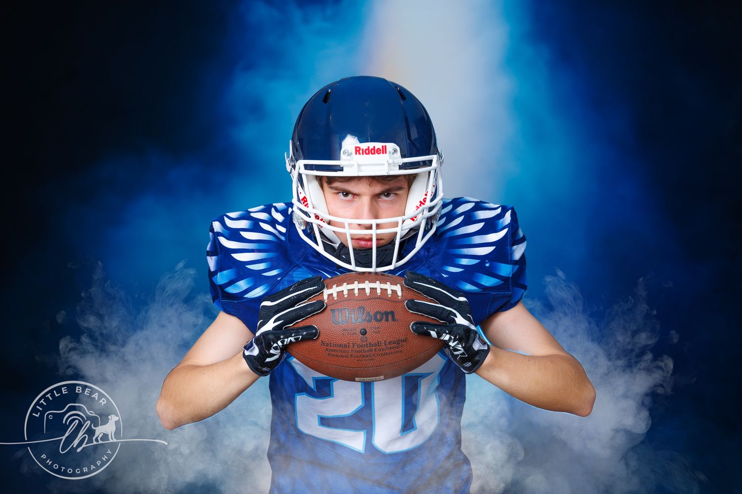 Young Hawkeyes football player #20 holding ball close in blue uniform surrounded by dramatic blue smoke.