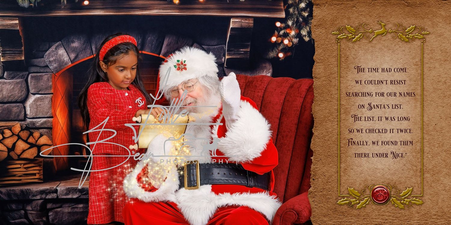 A young girl in red sits with Santa Claus by a fireplace, reading a Christmas list together in a festive holiday portrait.
